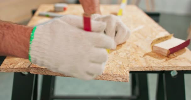 Närbild av en hårt arbetande professionell snickare som håller i en linjal och penna medan han mäter en bräda i en snickarverkstad. En skäggig DIY-entusiast mäter trä. Det finns ett låssmed bord och — Stockvideo