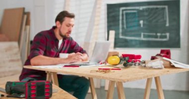 Dizüstü bilgisayardaki ilginç web sitesinden memnun olan genç adam kurslarda zanaatkarların atölyede vakit geçirmesi konusunda yetenekli tamirci müşterilerin siparişlerini netbook üzerinden kontrol ediyor.
