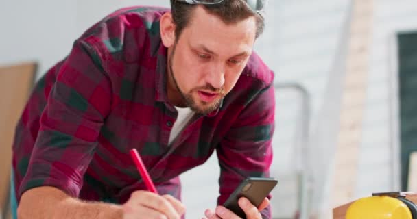 En skægget handyman analyserer designet på et stykke papir og smartphone Tømreren arrangerer detaljerne i ordren med klientens vittigheder og smil. – Stock-video