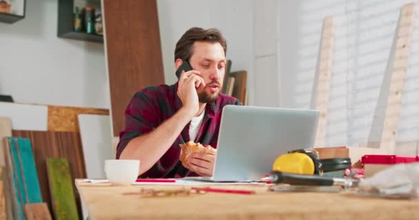 Portret nowoczesnego brodatego mężczyzny rozmawiającego przez telefon z klientem uśmiechającym się i robiącym notatki w stolarni Stolarz układa szczegóły zamówienia z dowcipami i uśmiechami klienta — Wideo stockowe