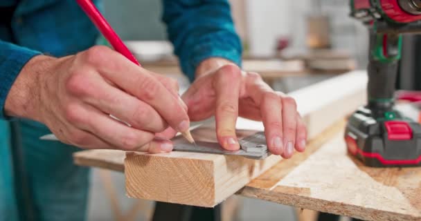 大工のワークショップでボードを測定しながら、定規と鉛筆を保持する勤勉なプロの大工のクローズアップ。ひげを生やしたDIY愛好家は木材を測定します。鍵屋のテーブルがあって — ストック動画