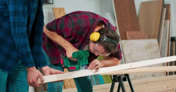 Νεαρός ξυλουργός κόβει μια σανίδα οστού με ένα παζλ Craftsmans χέρια σε ύφασμα προστατευτικά γάντια Η λεπίδα παζλ κόβει ακριβώς — Αρχείο Βίντεο