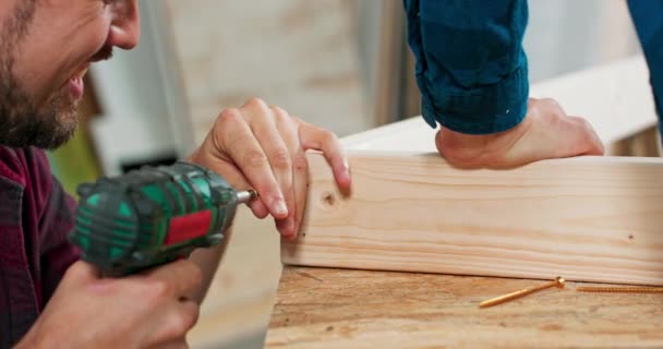 Συμπυκνωμένο νεαρό γενειοφόρο παθιασμένο ξυλουργό οδηγεί μια βίδα ξυλουργικής σε μια δοκό κατασκευής με ένα κατσαβίδι σε ένα εργαστήριο ξυλουργικής — Αρχείο Βίντεο
