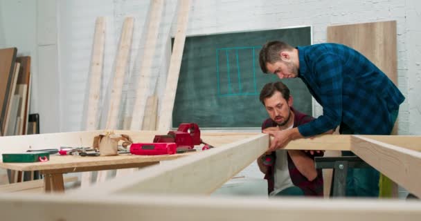 Jonge timmerlieden bouwen een massief houten muur in een timmerwerkplaats — Stockvideo