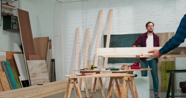Молодые плотники строят стену из массива дерева в столярной мастерской плотники передвигают стену на другую сторону, чтобы скрутить ее — стоковое видео