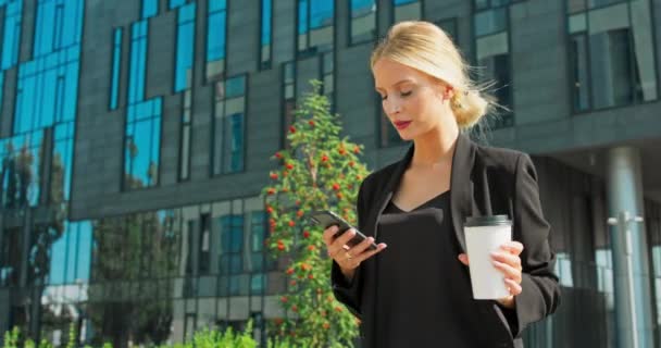 Hermosa mujer va a trabajar con café caminando cerca del edificio de oficinas Retrato de negocios exitosos — Vídeos de Stock