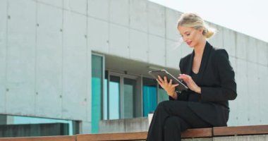 Yan görüntüde Young gülümseyen siyah ceketli çekici bir kadın dışarıda oturuyor ve tablet kullanıyor.
