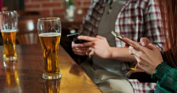 Homem está digitando uma mensagem em um smartphone em um bar, enquanto um copo de — Vídeo de Stock