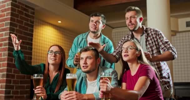 Разнообразная группа друзей смотрит телевизор в баре — стоковое видео