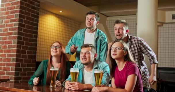 Caucasianos caras e meninas sentados no pub com cerveja à noite e assistindo jogo esporte — Vídeo de Stock