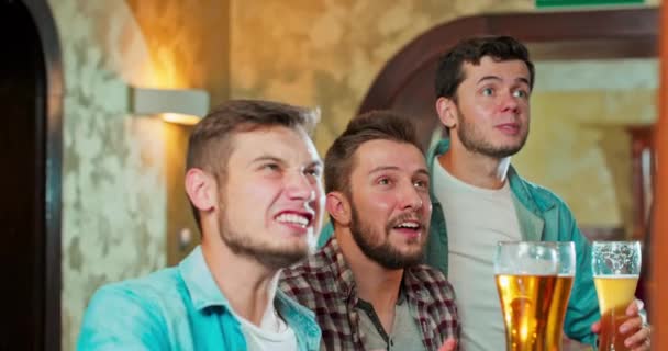 Nahaufnahme vor der Kamera charismatische, gut aussehende Typen in einer Kneipe, die sich ein Lieblingsspiel ansehen — Stockvideo