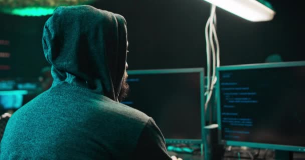 Disparo desde la espalda al hacker con capucha irrumpiendo en servidores de datos corporativos desde su subterráneo — Vídeo de stock
