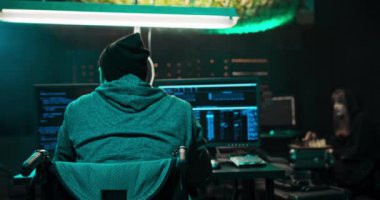 Tekerlekli sandalyedeki bir adam, kapüşonlu bir hacker bilgisayar üzerinde çalışıyor.