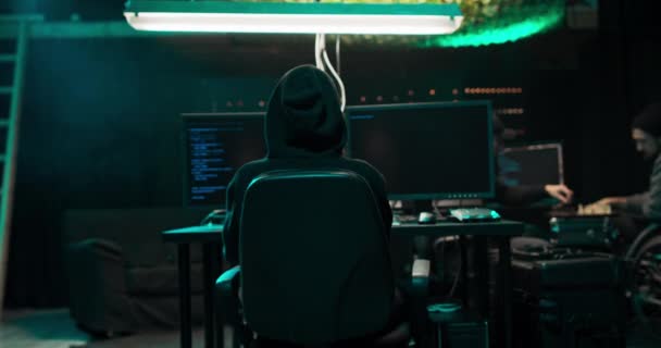 Shot from the Back to Hooded Hacker Breaking into Corporate Data Servers from His Underground — Stock video