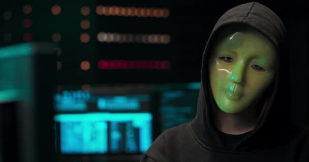 Gezocht hacker met gemaskerd gezicht kijkt in de camera in de achtergrond zijn operatiekamer — Stockvideo