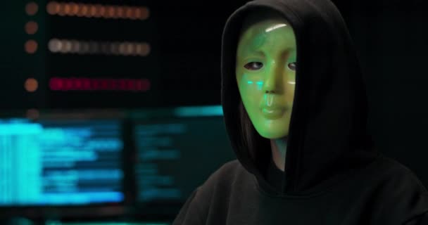 Close-up shot van een gemaskerde hacker in een hoodie zittend in het midden van de gegevens — Stockvideo