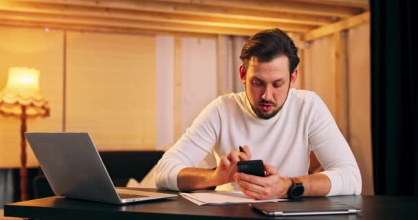 Midaldrende mand med bærbar computer, der arbejder eksternt fra hjemmet, ved hjælp af telefon og ser på netbook – Stock-video