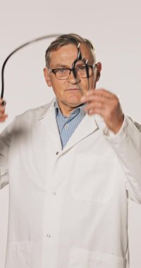 Beyaz tıbbi önlüklü yaşlı bir doktor boynuna steteskop takıyor. Erkek.