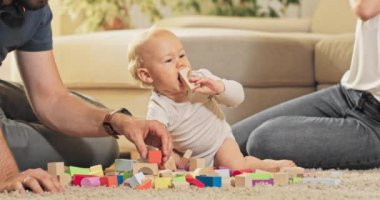 Ebeveynler çocuklarıyla birlikte halıda oturup tahta bloklarla oynarlar.,