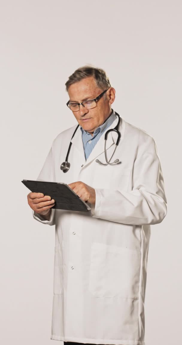 En moden læge, professionel, klædt i hvidt forklæde, skjorte, med briller og et stetoskop rundt – Stock-video