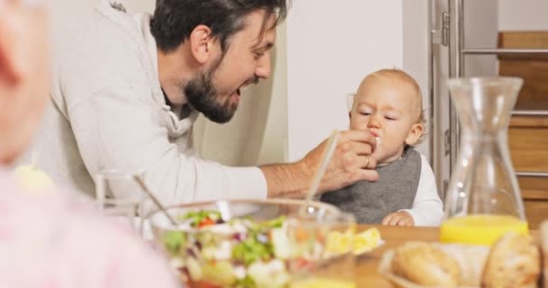 Jovem pai, homens sorridentes, senta-se ao lado da criança na cadeira de alimentação, alimenta filho com rolo, — Vídeo de Stock
