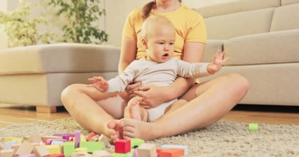 Ältere Schwester kümmert sich um Bruder, sie sitzt auf Teppich im Wohnzimmer und hält Kleinkind — Stockvideo