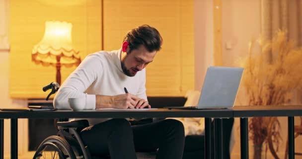 Hombre guapo caucásico discapacitado en un cuello alto blanco en silla de ruedas trabajando en la oficina del loft Hombre — Vídeos de Stock