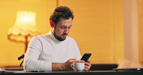 Bel homme hispanique sur un fauteuil roulant textos sur son smartphone tout en se relaxant à la maison — Video
