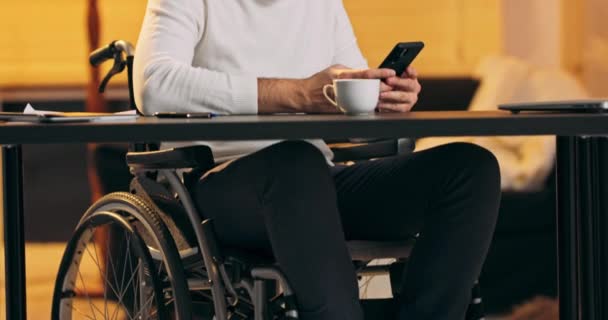 Muž tisíciletí v invalidním vozíku drží moderní smartphone textové zprávy v kanceláři Mladý podnikatel pomocí užitečné — Stock video