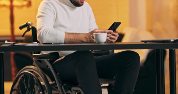 Joven emprendedor en lectura de sillas de ruedas y mensaje de escritura en el teléfono inteligente mientras trabaja en casa — Vídeos de Stock