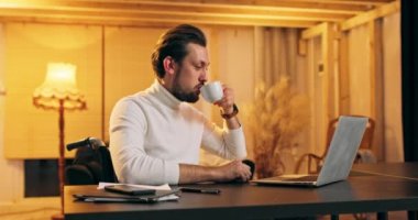 Evde dizüstü bilgisayar kullanırken kahve içen engelli bir adam. Genç profesyonel bir erkek bilgisayar kullanıyor.
