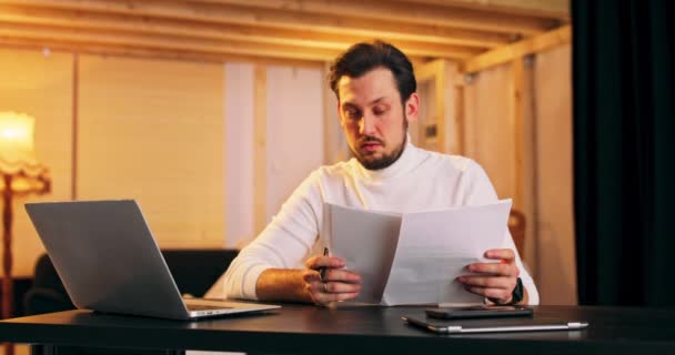 Élégant concentré caucasien mâle regarde sur certains documents, asseyez-vous à l'espace de travail à côté de loft — Video