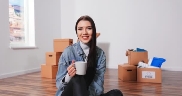 Allegro donna caucasica seduta sul pavimento soggiorno con una tazza di caffè e pensando a — Video Stock