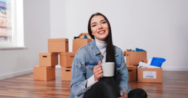 Allegro donna caucasica seduta sul pavimento soggiorno con una tazza di caffè e pensando a — Video Stock