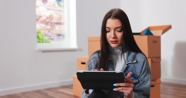 Joyeux belle jeune femme assise sur le sol dans un nouvel appartement et pensant à l'avenir — Video