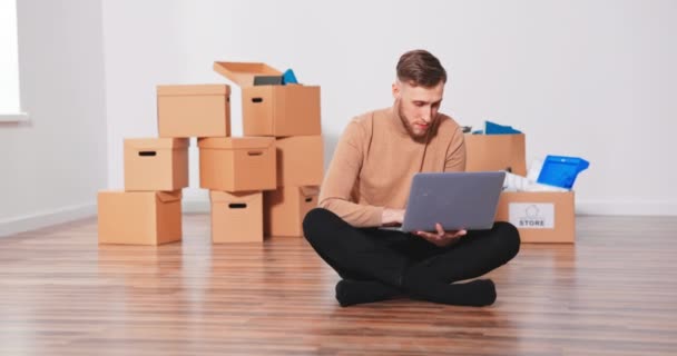 Confused Caucasian handsome young teenage boy sitting on the floor in new apartment and thinking — Stock Video