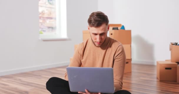 Smiling Caucasian handsome young teenage boy sitting on the floor in new apartment and thinking — Stock Video