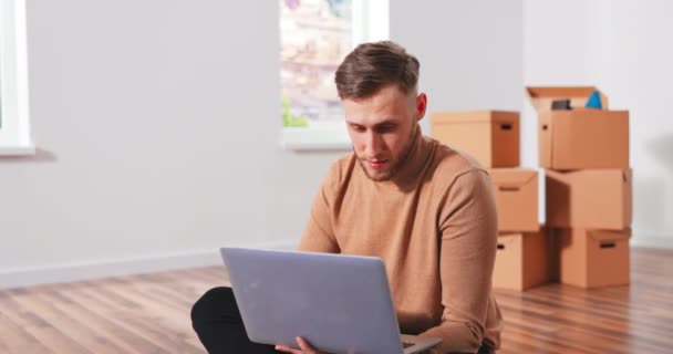 Smiling Caucasian handsome young teenage boy sitting on the floor in new apartment and thinking — Stock Video