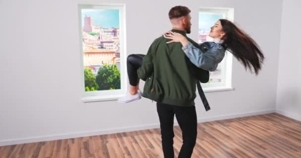 Jovem casal feliz em seu recém-comprado, apartamento alugado, namorado carrega sua namorada, gira e — Vídeo de Stock
