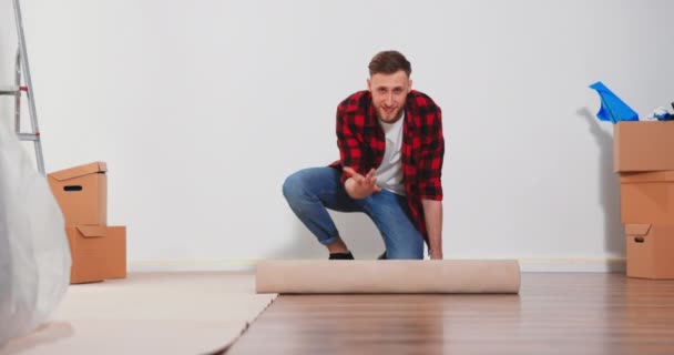 Un giovane apre un rotolo di cartone per proteggere il pavimento dalla pittura — Video Stock