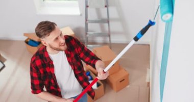 Yan görüş. Ev tadilatı sırasında beyaz tenli tamirci duvarları paten fırçasıyla boyuyor. Daire dekorasyonu ve... 