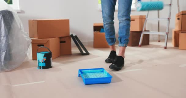 Blanke man bereidt zich voor op reparaties in nieuw appartement en zet roller in container met groen — Stockvideo