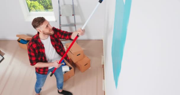Vista lateral. Parede de pintura handyman caucasiano com escova de rolo durante a renovação da casa. Apartamento redecoração e — Vídeo de Stock