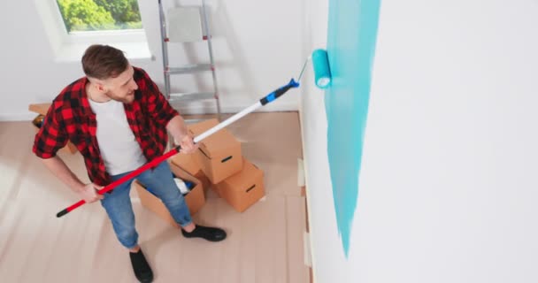 Bovenaanzicht. Blanke klusjesman schilderen muur met roller borstel tijdens woningrenovatie. Appartement herinrichting en — Stockvideo