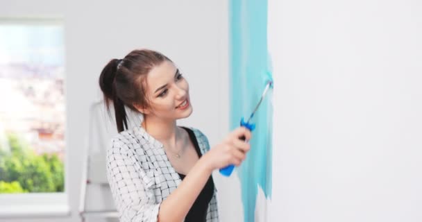 Молода красива кавказька щаслива жінка посміхається і малює стіну зеленим кольором, тримаючи роликову щітку — стокове відео