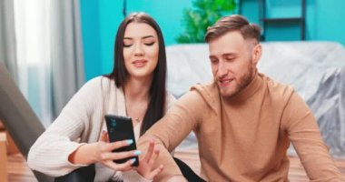 Mutlu çift kiracıları kiracılar taşınma günü yere oturur cep telefonu kullanır. 