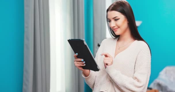 Sonriente milenial mujer de pie utilizando el gadget de almohadilla moderna en casa navegar por Internet o ir de compras, feliz — Vídeo de stock