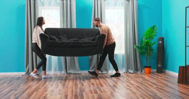 Un jeune couple heureux apporte un canapé à leur nouvelle maison. Ils s'assoient. — Video