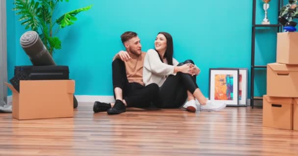 Zamknij młodą parę w nowym mieszkaniu. Mężczyzna i kobieta siedzący na podłodze — Wideo stockowe