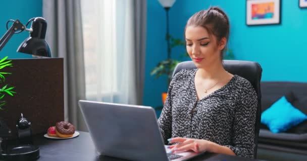 Een jong mooi brunette meisje maakt gebruik van een laptop terwijl zitten aan een bureau in een — Stockvideo